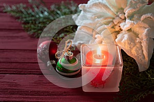 Christmas table centerpiece still life with a lighted candle, ornaments, white poinsettia, all on rustic red board background.  It