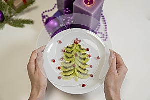 Christmas table decoration. kiwi and pomegranate in the shape of a christmas tree on a platter and purple candles