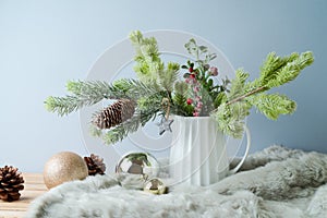 Christmas table decoration with pine tree branches in vase and ornaments over bright background