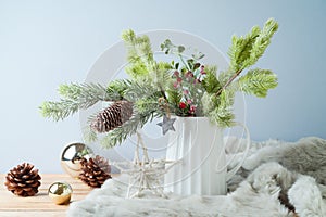 Christmas table decoration with pine tree branches in vase and ornaments over bright background