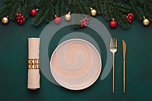 Christmas table with decorations. Empty plate, fork, knife. Gold cutlery, dark green background. Top view. Celebration place