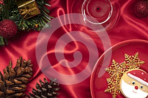 Christmas table decorations with a plate of sugar coated biscuit and a scented candle on bright red silk cloth