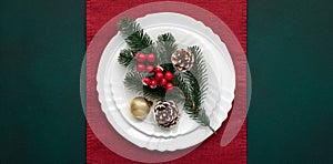 Christmas table with decorations, white empty plate on red tablecloth, green background, top view, above. Celebration xmas eve: