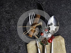 Christmas table place setting, cutlery in burlap bag with festive decorations star, cinnamon stick, pinecone with snow, berries,