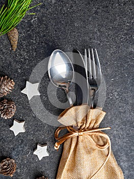 Christmas table place setting, cutlery in burlap bag with festive decorations star, golden bow, pinecone with snow, green branch