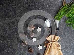 Christmas table place setting, cutlery in burlap bag with festive decorations star, golden bow, pinecone with snow, green branch