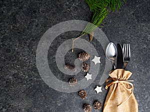 Christmas table place setting, cutlery in burlap bag with festive decorations star, golden bow, pinecone with snow, green branch