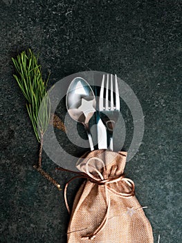 Christmas table place setting, cutlery in burlap bag with festive decorations wooden star, golden bow, pinecone, green branch .