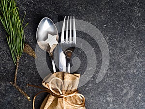 Christmas table place setting, cutlery in burlap bag with festive decorations wooden star, golden bow, pinecone, green branch .