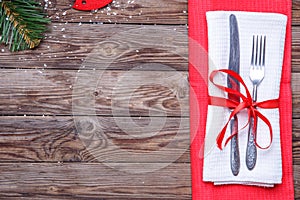 Christmas table place setting with fork and knife, decorated red ribbon and bow and red and white napkins.