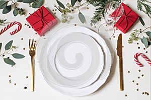 Christmas table place setting. Golden cutlery, porcelain plate, champagne glass, fir tree, eucalyptus branches, red gift