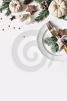Christmas table place setting. Golden cutlery, porcelain plate, fir tree branches, gift box, pine cones, confetti stars