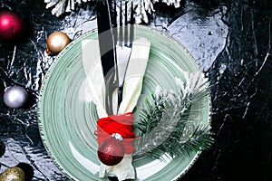 Christmas table place setting. Holidays background. Green plate, knife and fork with christmas decorations on black table. Top vie