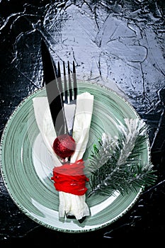 Christmas table place setting. Holidays background. Green plate, knife and fork with christmas decorations on black table. Top vie