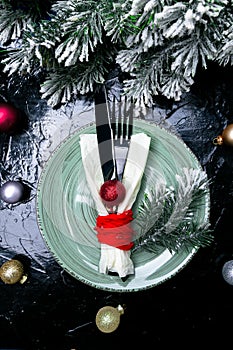 Christmas table place setting. Holidays background. Green plate, knife and fork with christmas decorations on black table. Top vie