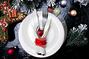 Christmas table place setting. Holidays background. White plate, knife and fork with christmas decorations on black table. Top vie