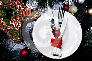 Christmas table place setting. Holidays background. White plate, knife and fork with christmas decorations on black table. Top vie