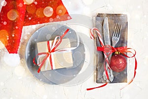 Christmas table place setting with napkin, fork, knife, ball, plate, candy canes, gift and santa hat
