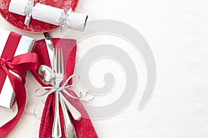 Christmas Table Place Setting in Red, White and Silver with Silverware, a gift, and party cracker on White Cloth Background with r photo