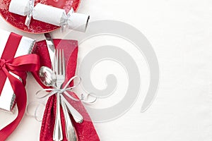 Christmas Table Place Setting in Red, White and Silver with Silverware, a gift, and party cracker on White Cloth Background with r