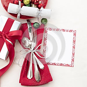 Christmas Table Place Setting in Red, White and Silver with Silverware, a gift, and party cracker on White Cloth Background with r