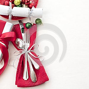 Christmas Table Place Setting in Red, White and Silver with Silverware, a gift, and party cracker on White Cloth Background with r