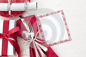 Christmas Table Place Setting in Red, White and Silver with Silverware, a gift, and party cracker on White Cloth Background with r