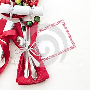 Christmas Table Place Setting in Red, White and Silver with Silverware, a gift, and party cracker on White Cloth Background with r