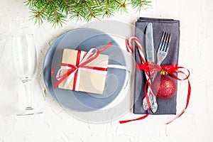 Christmas table place setting with tree fir branches, napkin, fork, knife, ball, plate, candy canes, gift and glass. Christmas