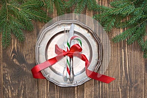 Christmas table setting with candy cane and red ribbon as decor, vintage dishware, silverware and decorations on board.