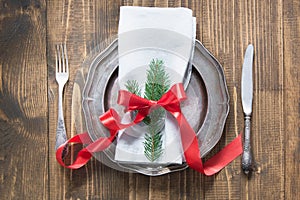 Christmas table setting with candy cane and red ribbon as decor, vintage dishware, silverware and decorations on wooden board.