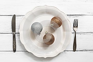 Christmas table setting. Christmas-tree balls on a white plate, knife, fork. White wooden rustic table. Top view, flat lay. The