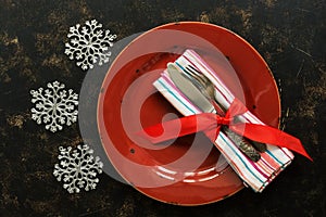 Christmas table setting, empty red plate, vintage cutlery on dark rustic background decorated with snowflakes.Top view, flat lay