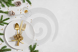 Christmas table setting with fir branches, golden decorations and cutlery on white background with copy space. New Year dinner.