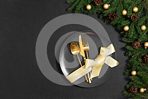 Christmas table setting with gold cutlery and bow in a plate on a black background. Happy new year. Space for text. Top view, flat