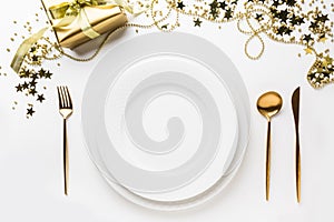 Christmas table setting with golden cutlery and decor on white background. Top view