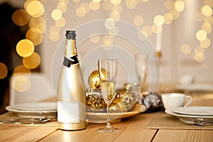 Christmas table setting with holiday decorations in a gold color. New Year celebration. A bottle and glass of champagne