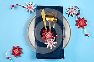 Christmas table setting with modern dishware and decorations on blue background. Top view. New Year place setting