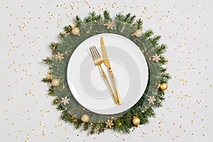 Christmas table setting with a New Year wreath, golden cutlery and confetti on a gray background. Top view, flat lay