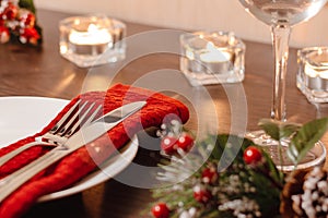 Christmas table setting. Plate and cutlery on napkin. Preparing for festive dinner. Candles burning on table on