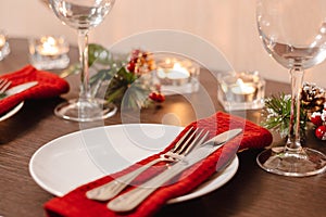 Christmas table setting. Plate and cutlery on napkin. Preparing for festive dinner. Candles burning on table on