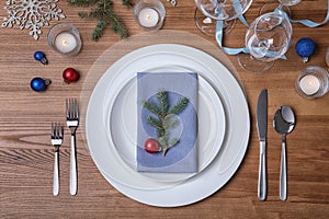 Christmas table setting with plates, cutlery, napkin and festive decor on wooden background