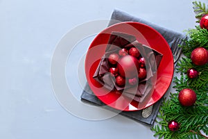 Christmas table setting with red plate, brown napkin in lotus shape and balls on gray wooden background. Holiday decorations