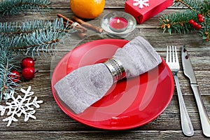 Christmas table setting. Red plate, napkin, fork, knife, branch of a tree on a wooden table