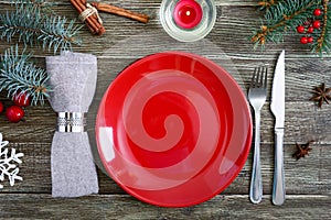 Christmas table setting. Red plate, napkin, fork, knife, branch of a tree on a wooden table
