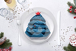 Christmas table setting white color with black silverware, napkin folded as a Christmas tree, Christmas silver balls, champagne,