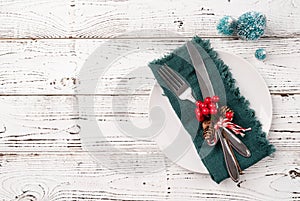 Christmas table setting with white dishware, silverware and red and green decorations on white wooden background. Top