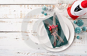 Christmas table setting with white dishware, silverware and red and green decorations on white wooden background. Top