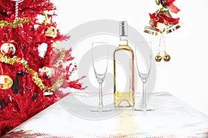 Christmas table with two glasses and a bottle of wine near a Christmas tree on a white background with bells. Christmas Concept