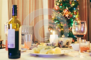 Christmas table with wine, food, candle and Christmas tree in the background. Mid focus.